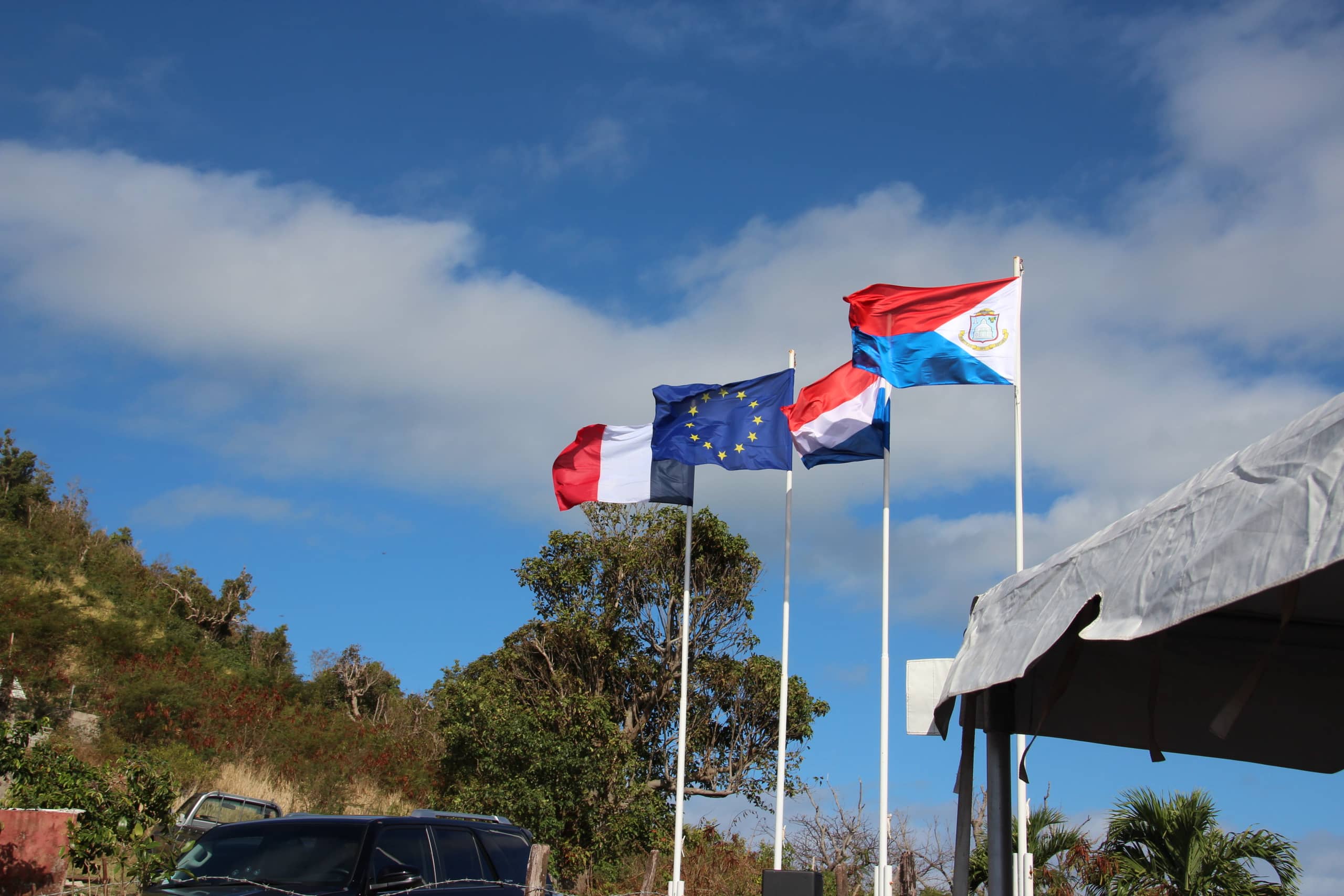 Four flags stand side by side: the flags of France, the EU, the Netherlands, and Sint Maarten.