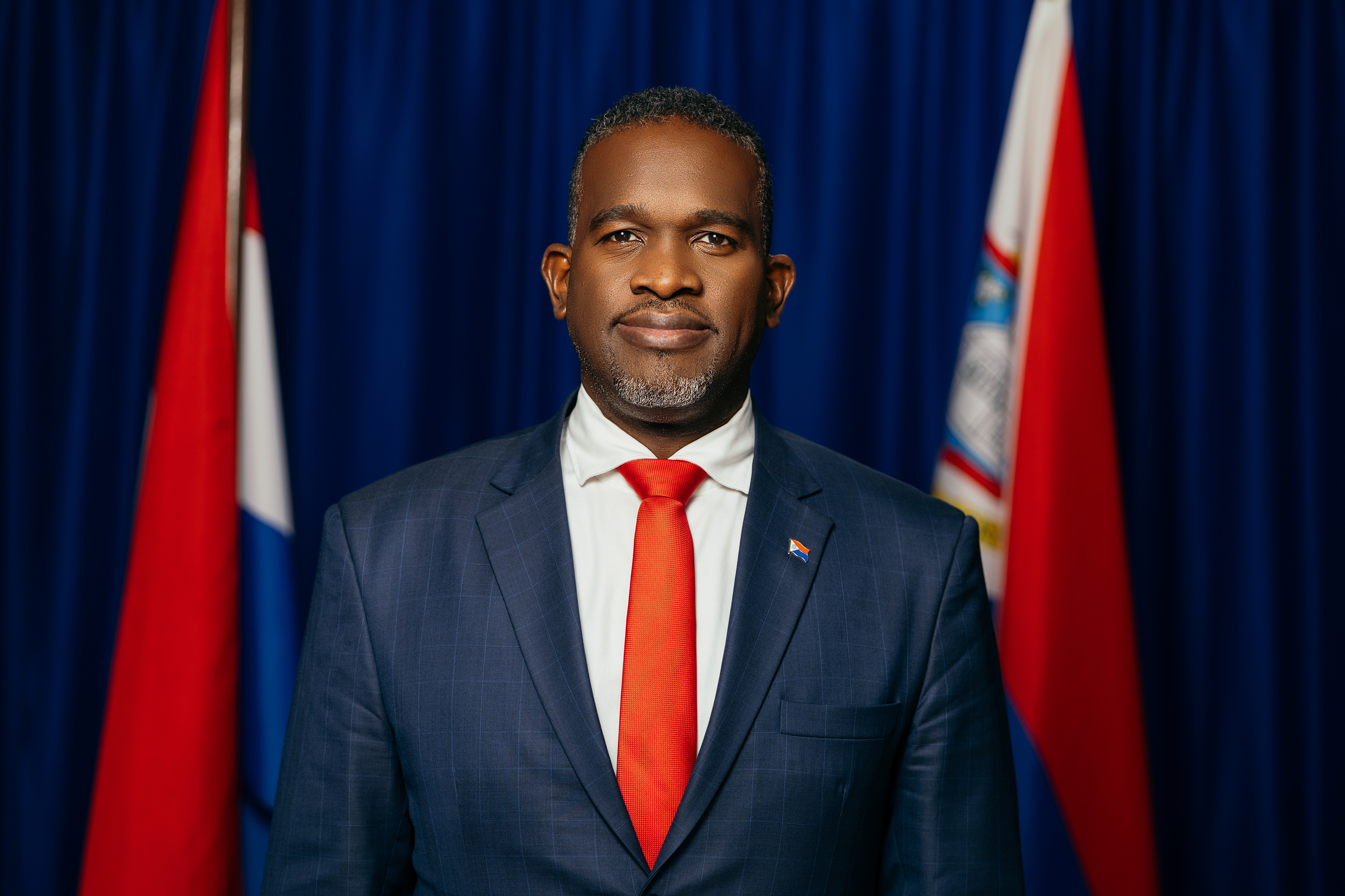 Official portrait of Governor Ajamu Baly in front of the flags of the Netherlands and Sint Maarten